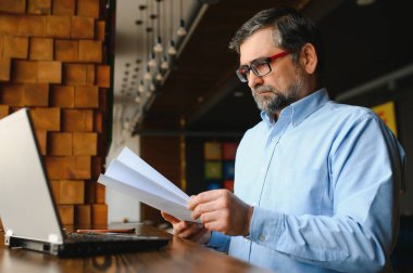 Erkek serbest yazar yeni bir iş projesi için bir kafede çalışıyor. Masadaki büyük bir pencerede oturuyor. Bir fincan kahveyle dizüstü bilgisayara bakıyor..