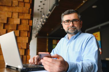 Erkek serbest yazar yeni bir iş projesi için bir kafede çalışıyor. Masadaki büyük bir pencerede oturuyor. Bir fincan kahveyle dizüstü bilgisayara bakıyor..