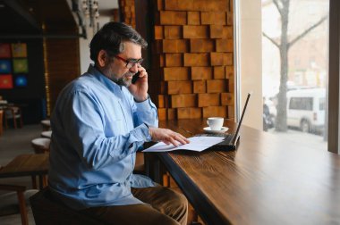 Erkek serbest yazar yeni bir iş projesi için bir kafede çalışıyor. Masadaki büyük bir pencerede oturuyor. Bir fincan kahveyle dizüstü bilgisayara bakıyor..