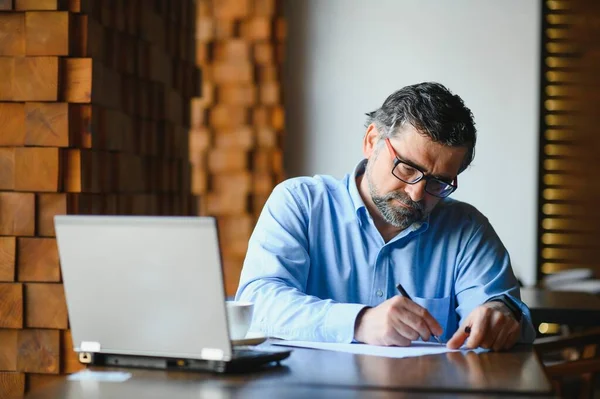 Kafede kahve içen olgun bir iş adamı. Güzel gözlükler takan, dizüstü bilgisayar kullanan, kameraya bakıp gülümseyen yakışıklı bir adamın portresi. Kahve molası.