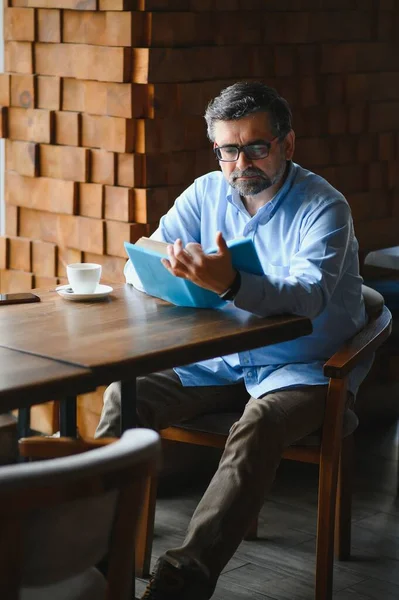 Bir kafede kitap okuyan yaşlı adam, edebi hobisi zevk.