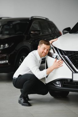 Araba galerisini ziyaret ediyorum. Yakışıklı sakallı adam yeni arabasını okşuyor ve gülümsüyor.