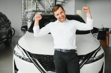 Gösteri odasındaki genç yakışıklı adam arabanın yanında duruyor..