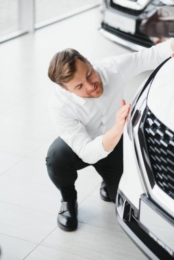 Mutlu yakışıklı sakallı adam galeriden araba alıyor, yeni arabanın kaputuna sarılıyor..