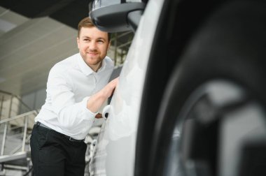 Araba galerisini ziyaret ediyorum. Yakışıklı sakallı adam yeni arabasını okşuyor ve gülümsüyor.