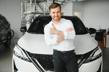 Gösteri odasındaki genç yakışıklı adam arabanın yanında duruyor..