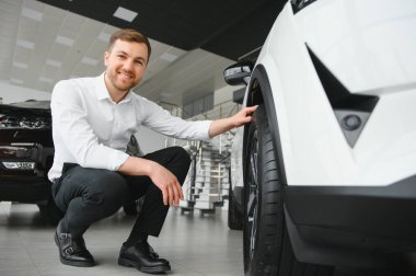 Araba galerisini ziyaret ediyorum. Yakışıklı sakallı adam yeni arabasını okşuyor ve gülümsüyor.