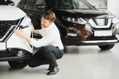 Araba galerisini ziyaret ediyorum. Yakışıklı sakallı adam yeni arabasını okşuyor ve gülümsüyor.