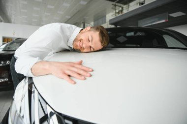 Araba galerisini ziyaret ediyorum. Yakışıklı sakallı adam yeni arabasını okşuyor ve gülümsüyor.