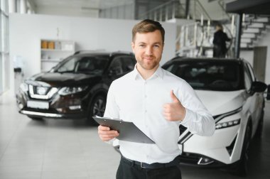 Araç arama asistanı. Bir pano tutan ve bir araba bayilik kamera bakarak formalwear yakışıklı bir genç araba satış elemanı Portresi.