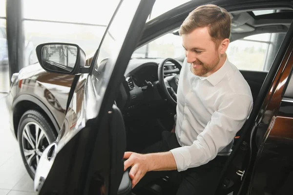 Man adult customer male buyer client wears classic suit white shirt chooses auto wants to buy new automobile touch check car in showroom vehicle salon dealership store motor show indoor. Sales concept