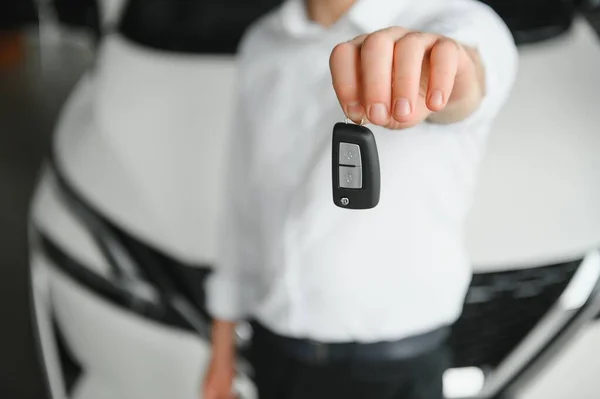 Close up of the car owner's hand holding the delivery key to buyers. Concept of selling cars and giving keys to new owners.