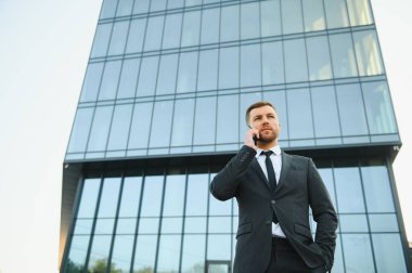 Modern iş adamı. Kendine güvenen, takım elbiseli genç bir adam arka planda şehir manzarasıyla dışarıda dikilirken gözlerini kaçırıyor..