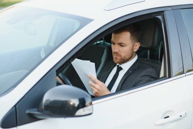 Tarz ve statü sahibi bir adam. Takım elbiseli yakışıklı genç adam araba kullanırken gülümsüyor..