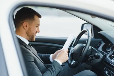 Her zaman acelen var. Takım elbiseli yakışıklı genç adam araba kullanırken gülümsüyor.