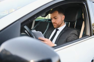 Her zaman acelen var. Takım elbiseli yakışıklı genç adam araba kullanırken gülümsüyor.