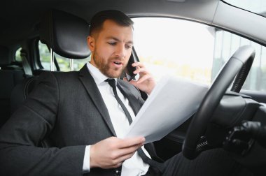 Tarz ve statü sahibi bir adam. Takım elbiseli yakışıklı genç adam araba kullanırken gülümsüyor..