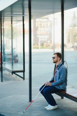 Beyaz bastonlu kör adam şehirde toplu taşıma bekliyor.