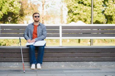 Kör adam parkta bankta kitap okuyor..