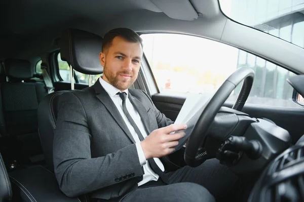 Man of style and status. Handsome young man in full suit smiling while driving a car.