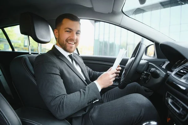 Man of style and status. Handsome young man in full suit smiling while driving a car.