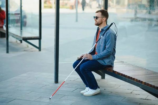 Blinded man waiting for bus at a bus station.