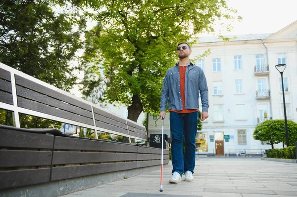 young blind man with white cane walking across the street in city.