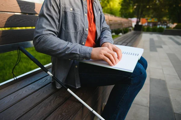 Blind man reading book on bench in park.