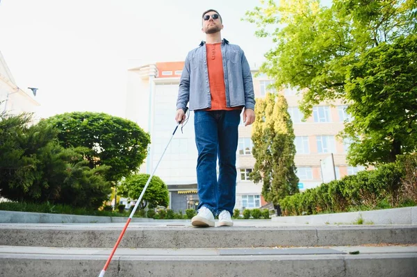 白いケトキを持つ若い盲目の男が街の通りを横切って歩いている — ストック写真