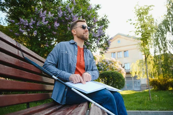 Blind man reading book on bench in park.