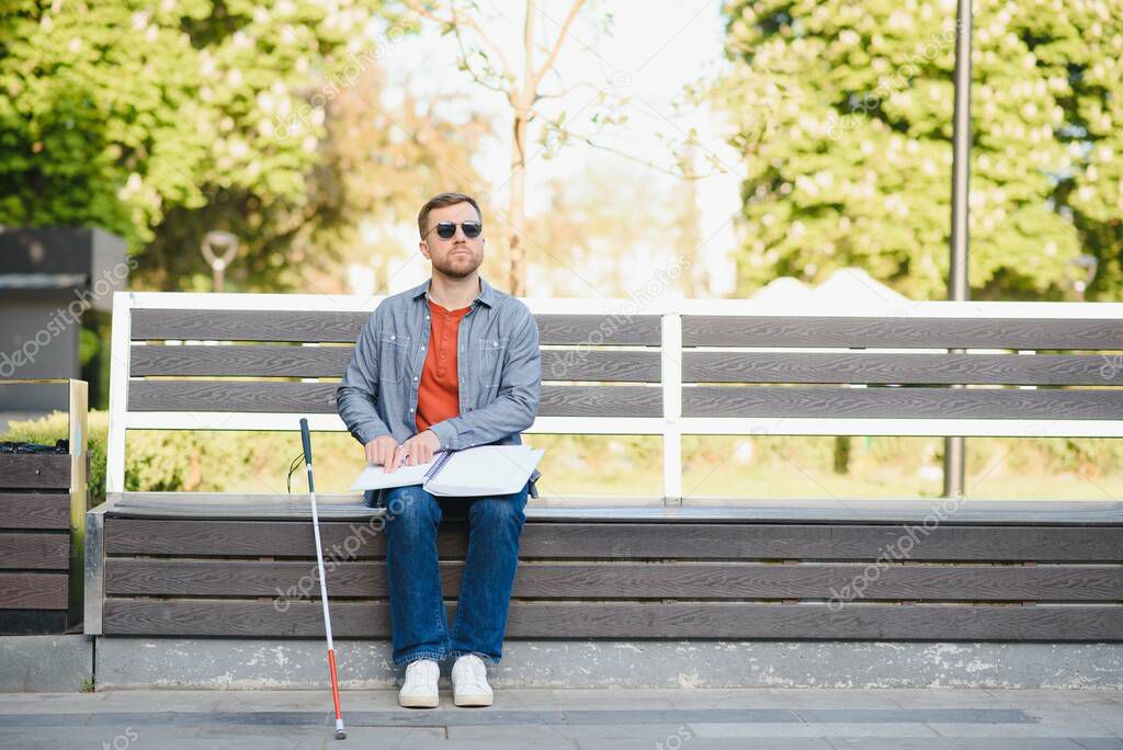 Blind man reading book on bench in park.