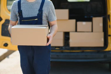Teslimat servisi çalışanı. Teslimat servisinde çalışan bir adamın portresi. Kutulu kurye portresi. Minibüsün yanındaki kurye. Teslimat servis kariyeri
