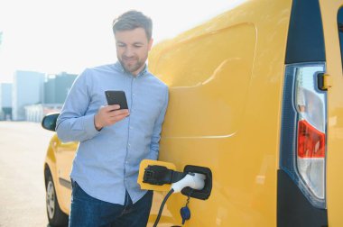 Adam şarj istasyonunda bir elektrikli arabayı şarj ediyor.