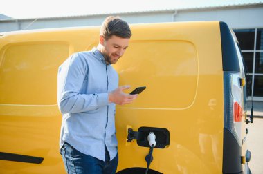 Adam şarj istasyonunda bir elektrikli arabayı şarj ediyor.