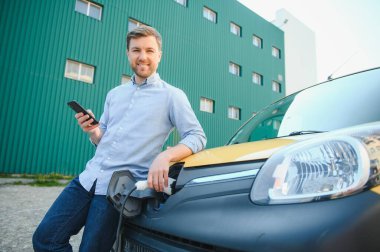 Adam şarj istasyonunda bir elektrikli arabayı şarj ediyor.