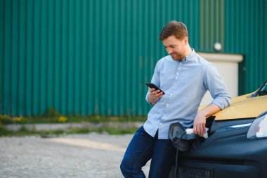 Gülümseyen adam araba şarj cihazını prizden.