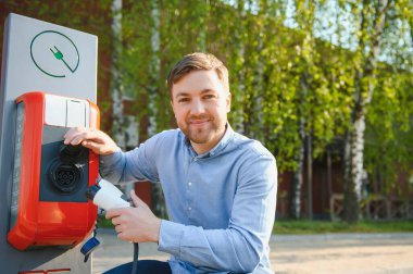 Adam şarj istasyonunda elektrikli arabasını şarj ediyor.