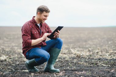 Tablet Mısır tarlasında baharda çömelme ile genç yakışıklı bir çiftçi. Tarım ve İnovasyon kavramı.