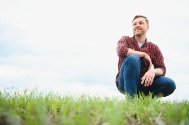 Genç bir çiftçi tarladaki buğday filizlerinin kalitesini kontrol eder. Tarım kavramı.