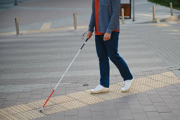 young blind man with white cane walking across the street in city.