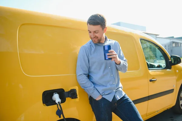 Schöner Mann Trinkt Kaffee Beim Laden Von Elektroautos — Stockfoto