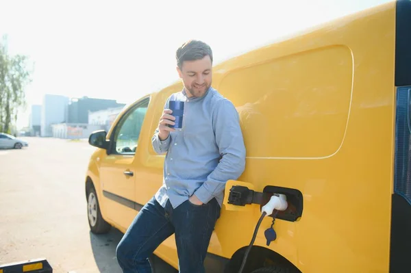 Schöner Mann Trinkt Kaffee Beim Laden Von Elektroautos — Stockfoto