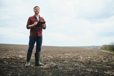 Botlu bir çiftçi baharda ekilmiş bir tarlada tabletiyle çalışır. Sonbaharda tarlada sürülen tarlaları değerlendiren bir tarım uzmanı. Tarım. Akıllı tarım teknolojileri.