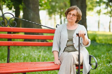 Tişörtlü zarif yaşlı kadın sıcak bir günde parkta bankta oturuyor..