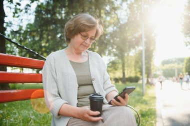 Yaşlı bir kadın yaz parkında bankta oturuyor..