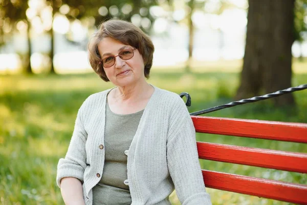 暖かい日に公園のベンチに座っているシャツのエレガントな高齢者の女性 — ストック写真