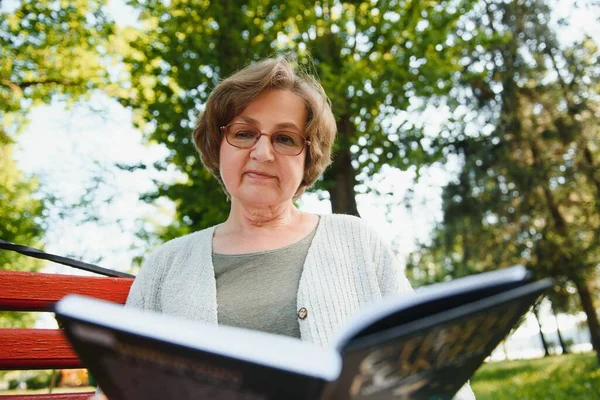 Retired woman reading a book on the bench.