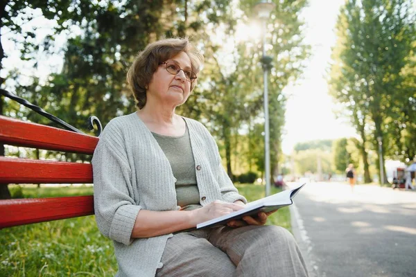 Retired woman reading a book on the bench.