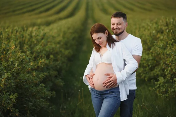 Happy and young pregnant couple hugging in nature.