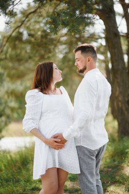 Mutlu ve genç hamile çift doğada sarılıyorlar..